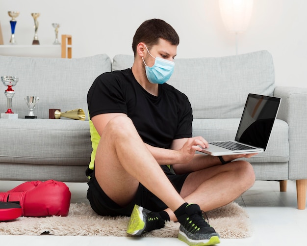 Man wearing a medical mask while holding a laptop