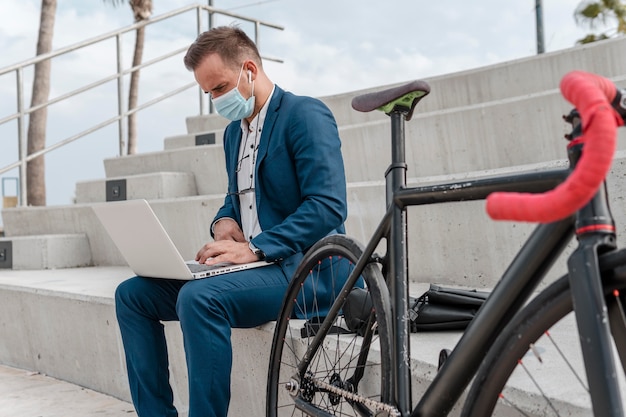 Foto gratuita uomo che indossa una maschera medica mentre è seduto accanto alla sua bici