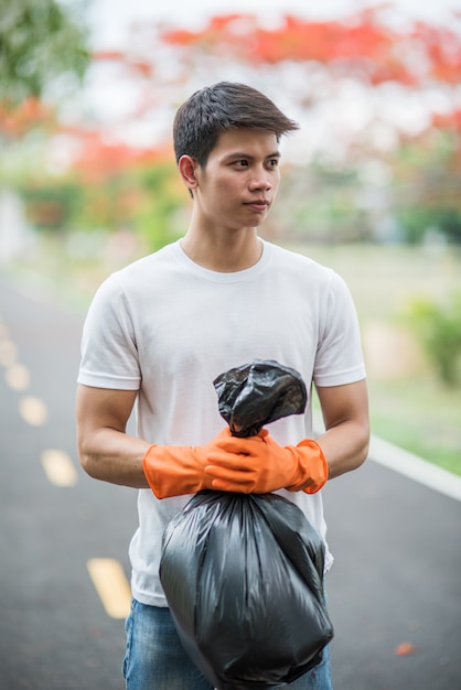 A man wearing orange gloves collecting garbage in a black bag.