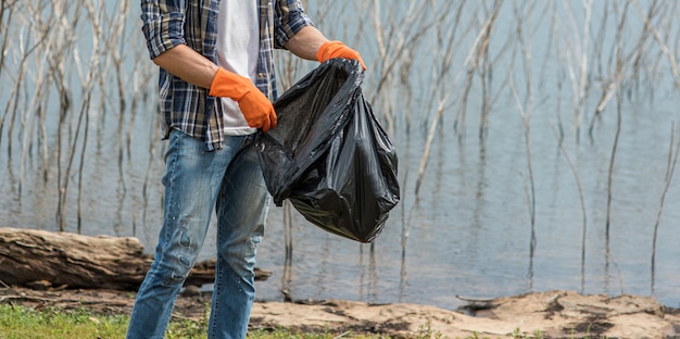 Free photo a man wearing orange gloves collecting garbage in a black bag.