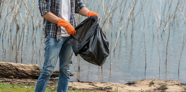 A man wearing orange gloves collecting garbage in a black bag.