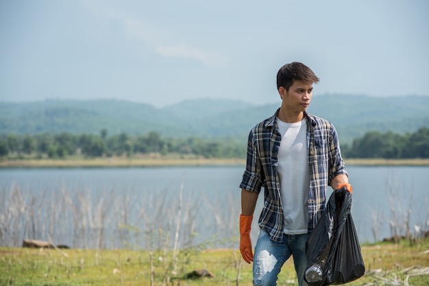 A man wearing orange gloves collecting garbage in a black bag.