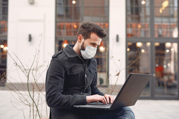노트북으로 도시에 앉아 보호 마스크를 착용하는 남자