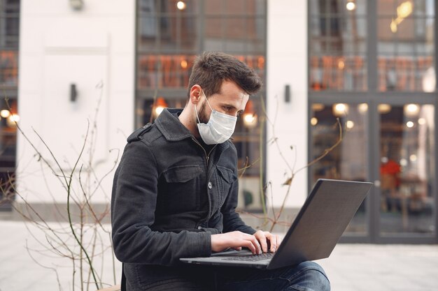 Man wearing a protective mask sitting in the city with a laptop