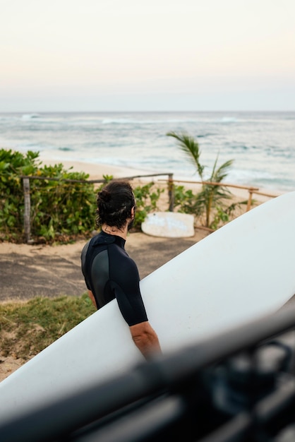 Man wearing surfer clothes and holding his surfboard