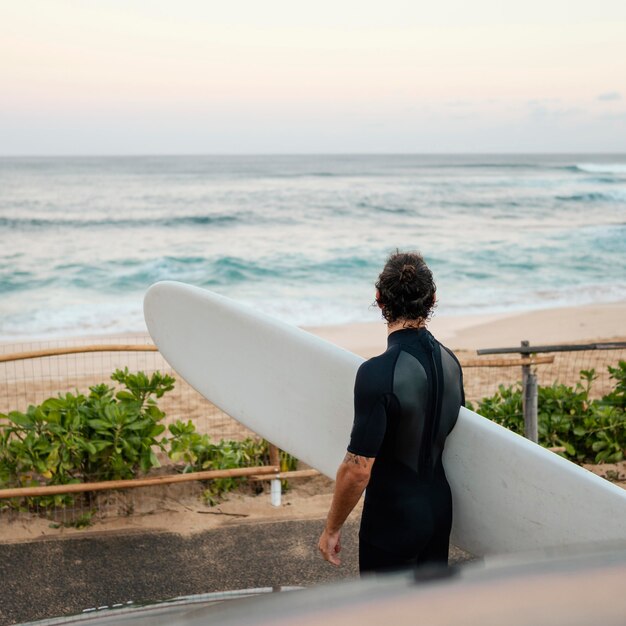 Man wearing surfer clothes and holding his surfboard