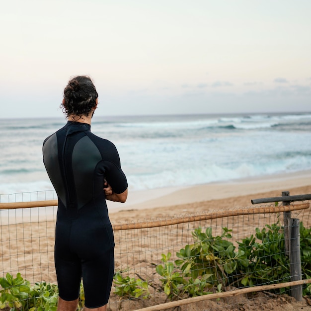 Foto gratuita uomo che indossa abiti da surfista e guardando il mare