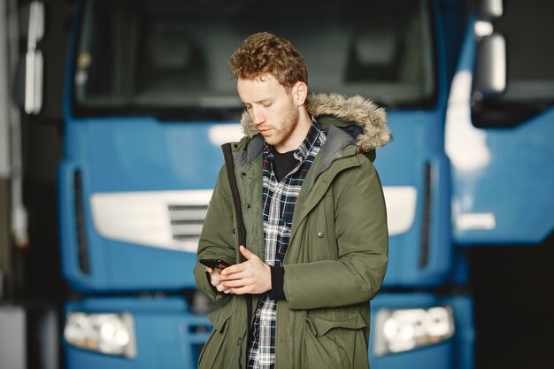 暖かい緑のジャケットを着ている男。ガレージに駐車したトラック。ロジスティクスの問題を解決する