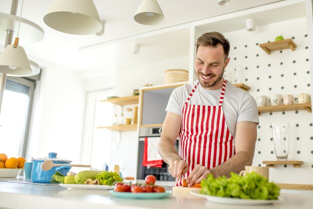 Man wearing a white apron with red lines and cooking something in the kitchen