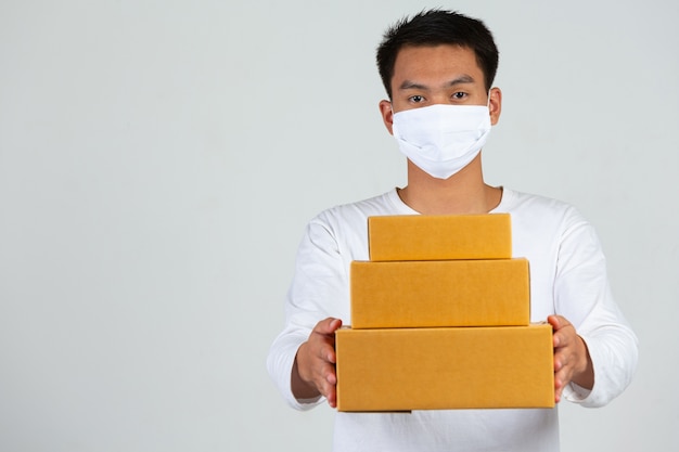 A man wearing a white t-shirt is holding a brown post box to deliver things Make gestures and facial expressions.