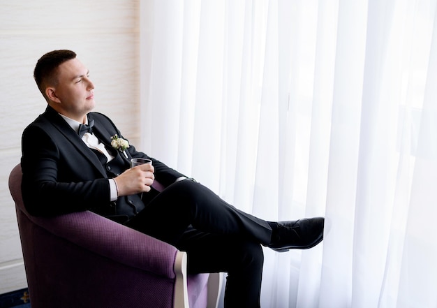 Free photo man in wedding suit with glass of whiskey indoors