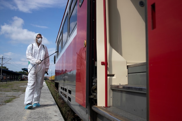 伝染性の高いコロナウイルスの拡散を防ぐために、地下鉄の電車の外壁を消毒および消毒する白い防護服を着た男