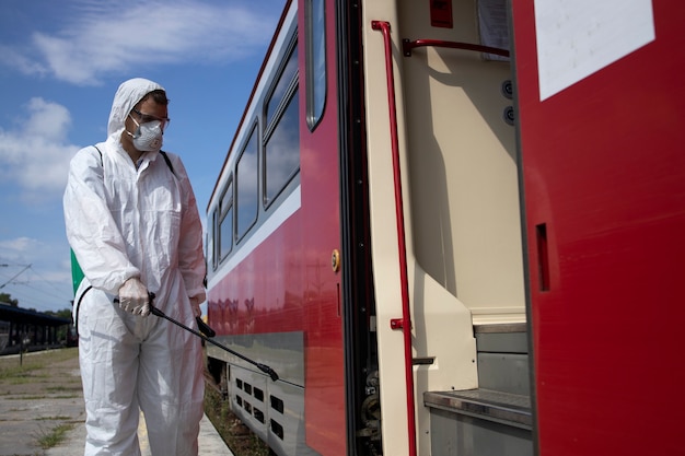 흰색 보호 복을 입은 남자가 전염성이 높은 코로나 바이러스의 확산을 막기 위해 지하철 열차 외부를 소독하고 살균합니다.