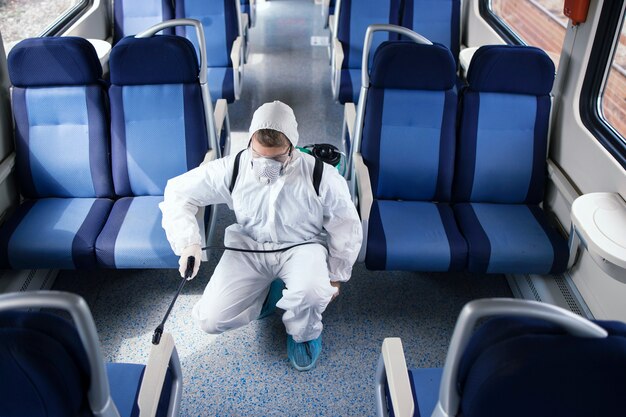 Man in white protection suit disinfecting and sanitizing subway train interior to stop spreading highly contagious corona virus