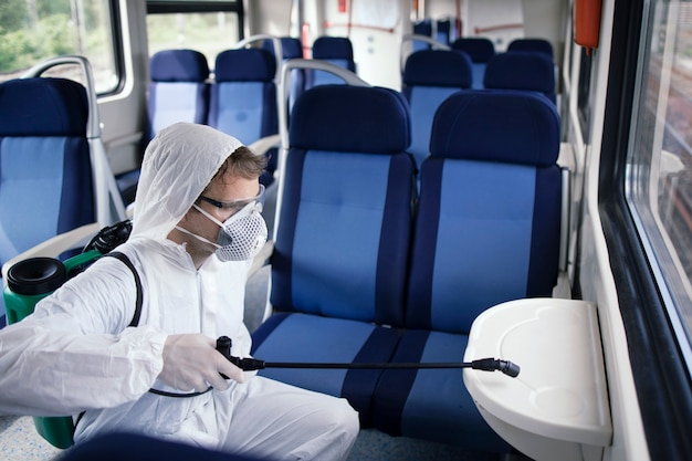 Man in white protection suit disinfecting and sanitizing subway train interior to stop spreading highly contagious corona virus