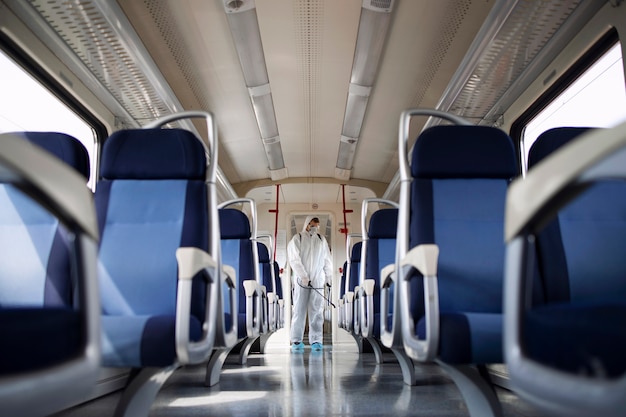 Man in white protection suit disinfecting and sanitizing subway train interior to stop spreading highly contagious corona virus