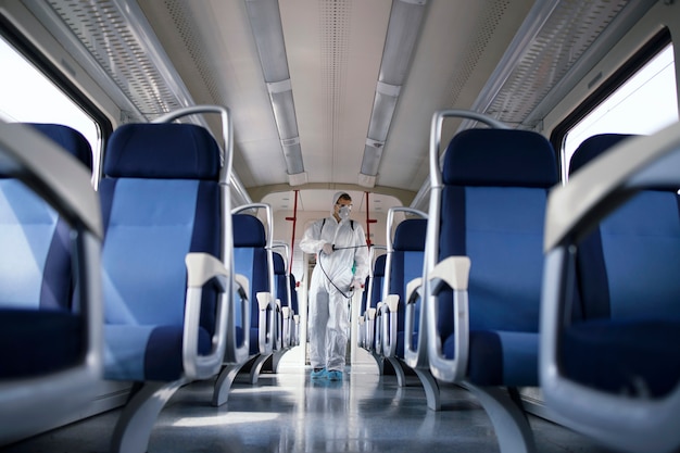 Man in white protection suit disinfecting and sanitizing subway train interior to stop spreading highly contagious corona virus