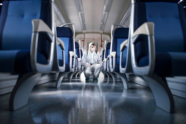 Man in white protection suit disinfecting and sanitizing subway train interior to stop spreading highly contagious corona virus