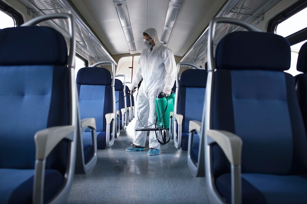 흰색 보호 복을 입은 남자가 전염성이 높은 코로나 바이러스의 확산을 막기 위해 지하철 열차 내부를 소독하고 살균합니다.