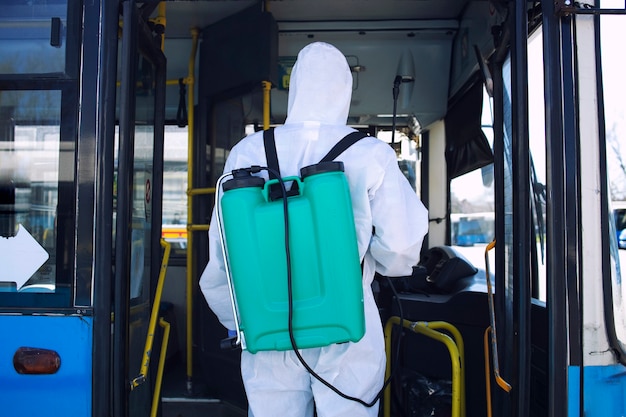 코로나 바이러스의 전염병으로 인해 저수지가 버스에 들어가 소독제를 뿌리는 흰색 보호 복을 입은 남자