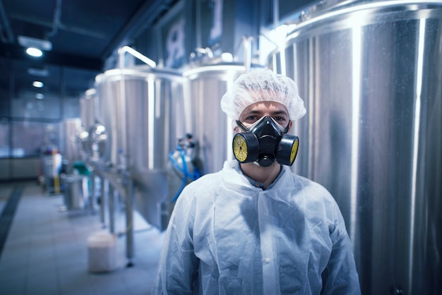 Man in white protective uniform with hairnet and protective mask handling hazardous chemicals