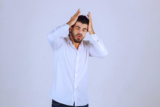 Man in white shirt coverin his face, feels sad and has headache.