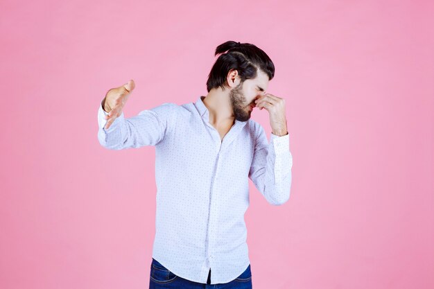 Man in a white shirt holding breath as he feels bad smell.