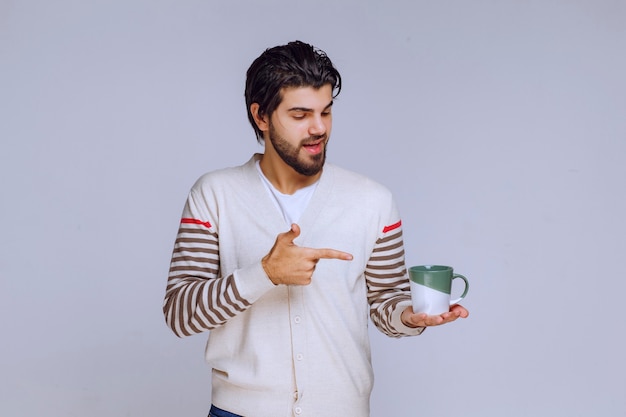 Man in white shirt holding a coffee cup and pointing at it. 