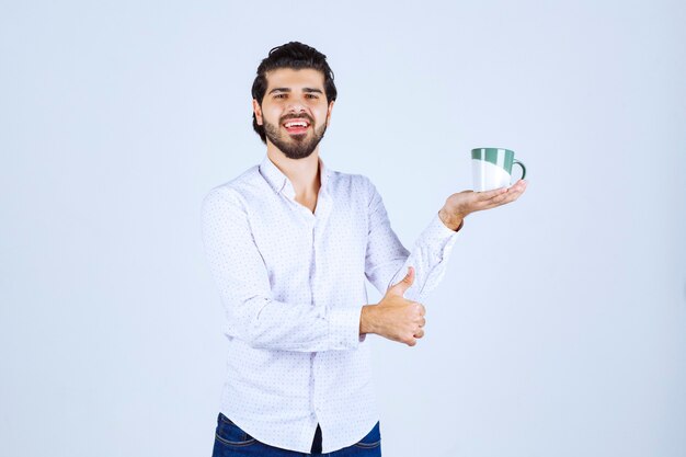 Man in a white shirt holding a coffee mug and enjoying it.