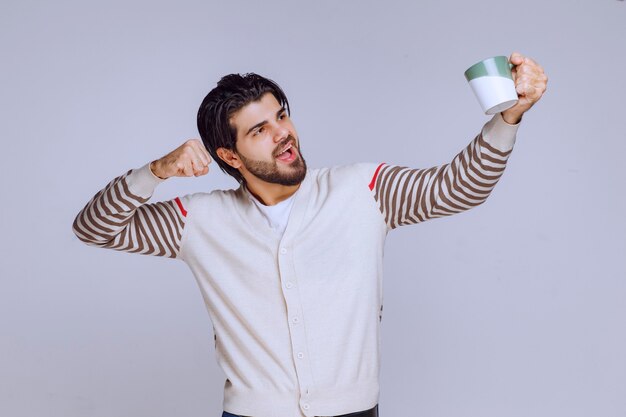 Man in white shirt holding a coffee mug and showing it. 