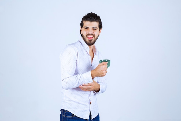 Man in a white shirt holding a cup of coffee and enjoying it