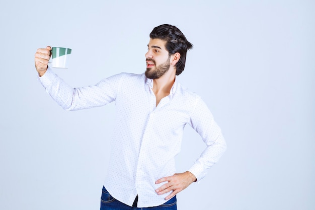 Man in a white shirt holding a cup of coffee and enjoying it