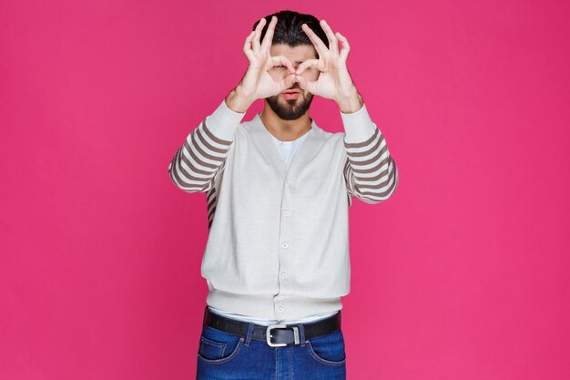 Man in white shirt looking through his fingers. 