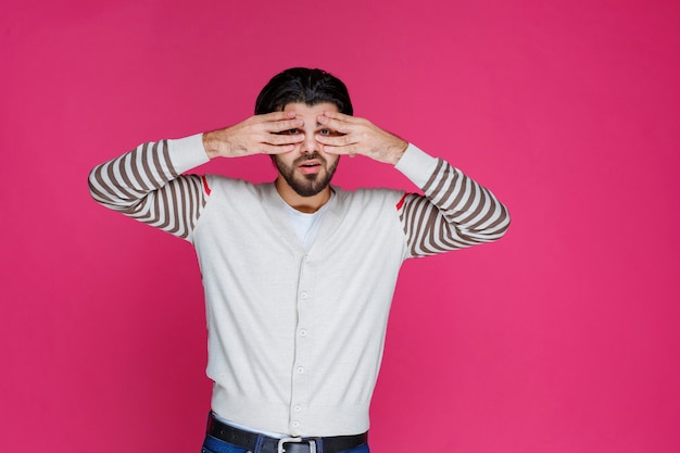 Man in white shirt looking through his fingers. 