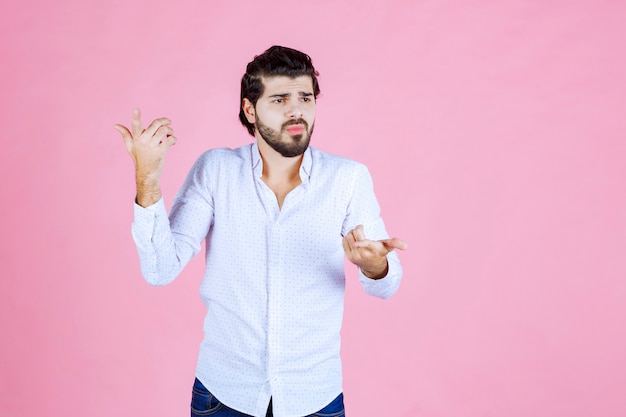 Man in a white shirt looks confused and trying to explain himself while using hand gests.