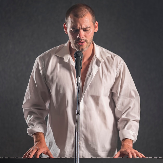 Человек в белой рубашке играет на клавишных и поет