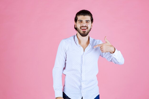 Uomo in una camicia bianca che indica se stesso.