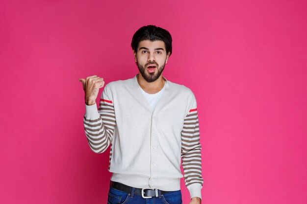 Man in white shirt pointing and presenting someting in the back. 