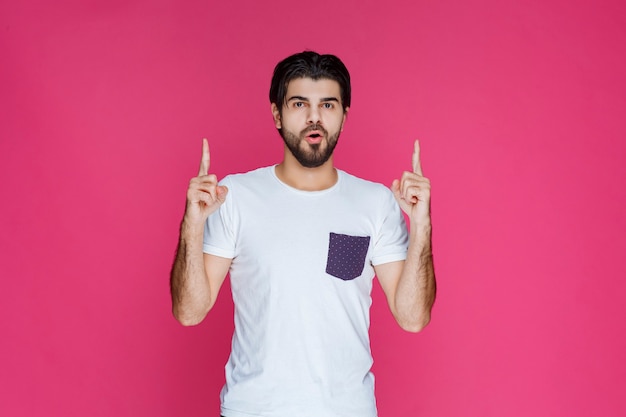 Free photo man in white shirt pointing to something above.