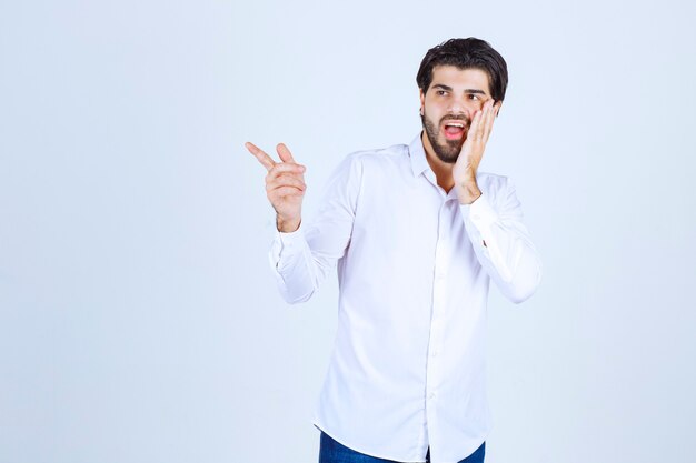 Man in white shirt pointing somewhere on the left with face emotions.