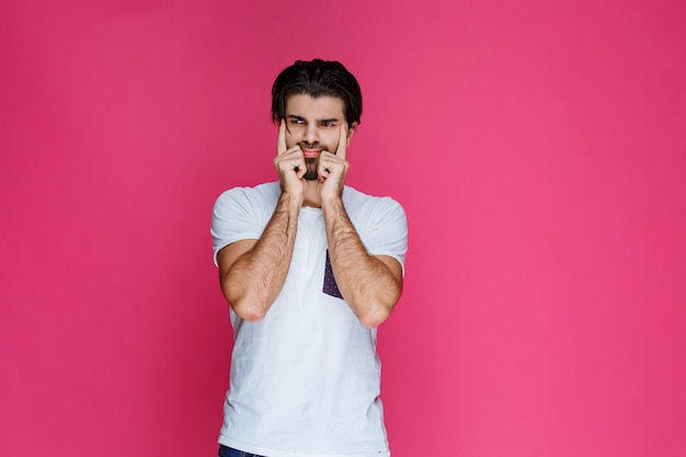 Man in white shirt putting his hand to his face and thinking.