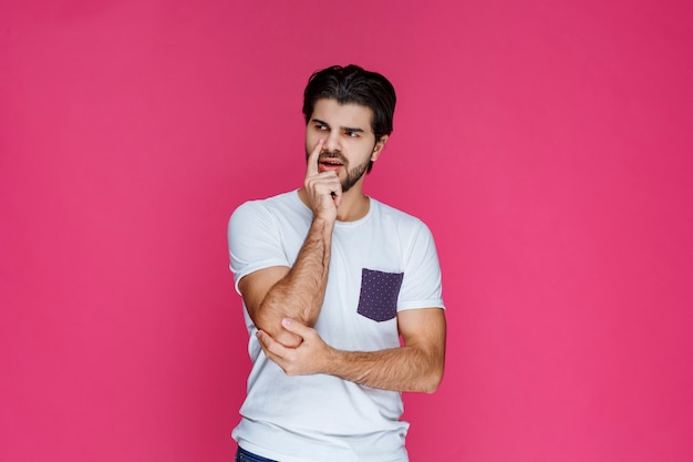 Uomo in camicia bianca che si mette la mano al viso e pensa.