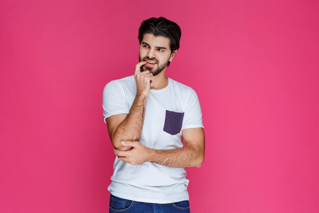 Man in white shirt putting his hand to his face and thinking.