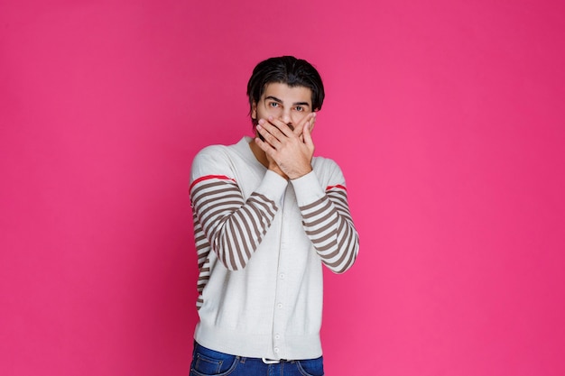 Man in a white shirt putting his hand to his face. 