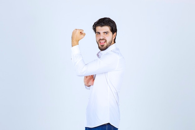Man in white shirt showing his arm muscles and fist.