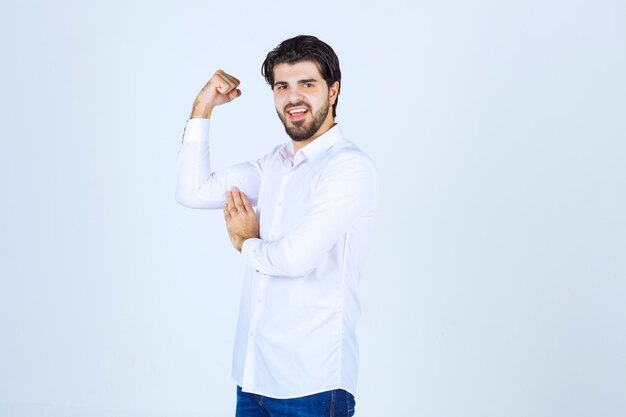 Человек в белой рубашке, показывая мышцы руки и кулак.
