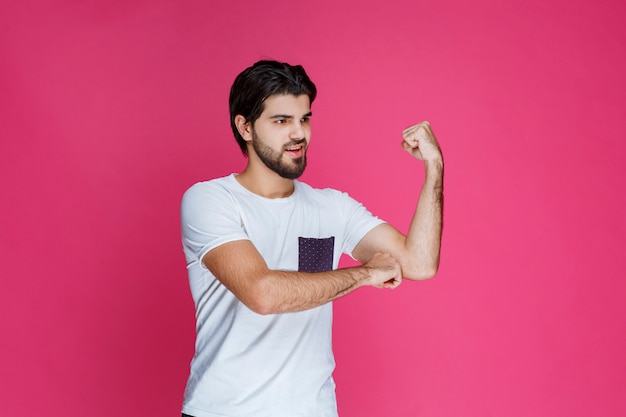 Man in white shirt showing his fist and biceps muscles.