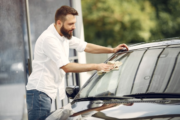 Man in a white shirt wipes a car in a car wash