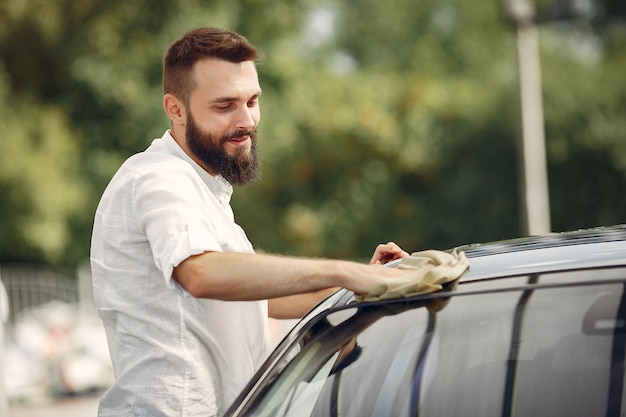 Man in a white shirt wipes a car in a car wash