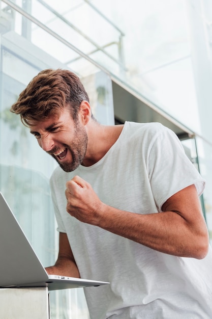 Free photo man in white t-shirt with laptop celebrating